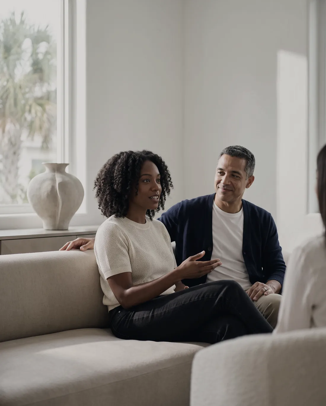 A couple on a sofa in a bright living room, mid-conversation with their advisor.