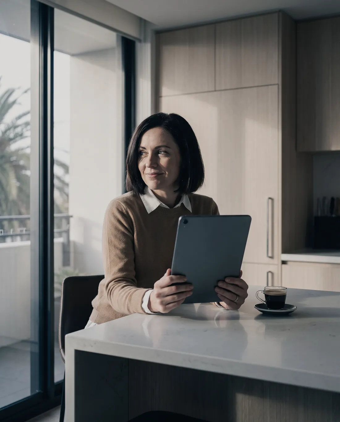 A woman at a kitchen island answers questions on a tablet, a cup of espresso beside her.