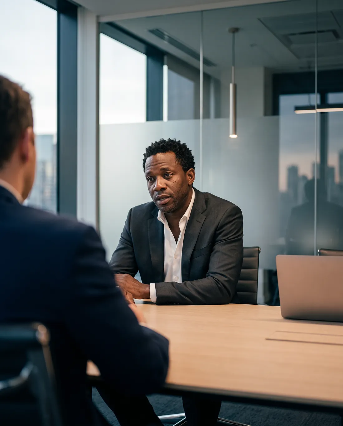 A founder in a charcoal suit leans in across a conference table, mid-conversation with an advisor.