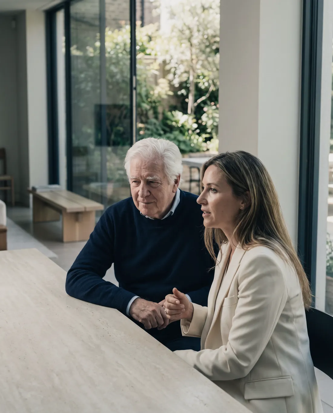 A father and his adult daughter at a stone table in a calm modern room, the daughter speaking.